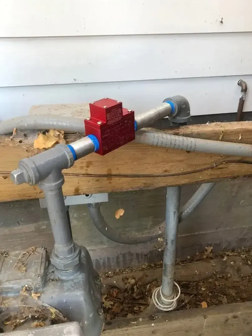 Red and gray plumbing valve assembly outdoors with copper pipes